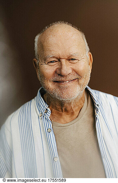 Portrait of smiling elderly man against brown background