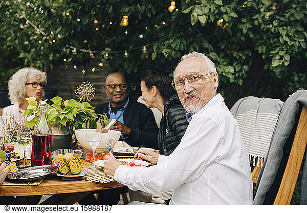 Portrait of smiling elderly man sitting with friends enjoying dinner at dining table