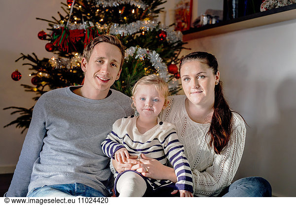 Portrait of smiling family sitting against Christmas tree at home