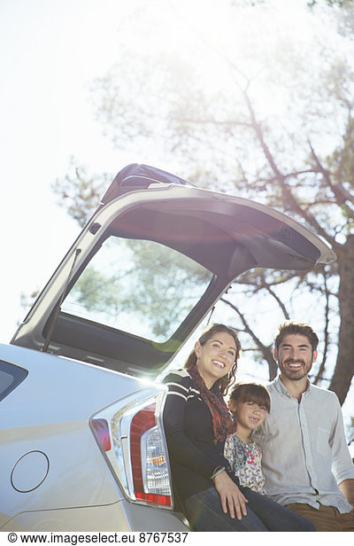 Portrait of smiling family sitting against rear of car