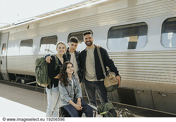 Portrait of smiling family standing with luggage in front of train at railroad station
