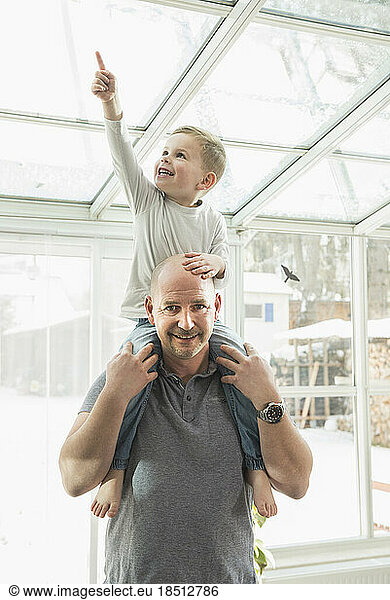 Portrait of smiling father carrying son on his shoulders at home
