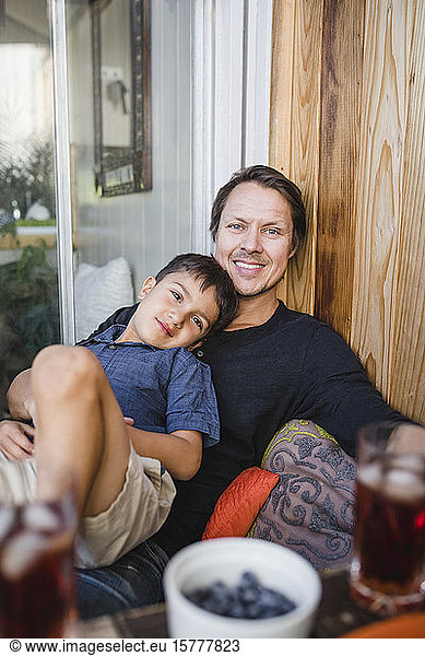 Portrait of smiling father with son sitting by wooden wall