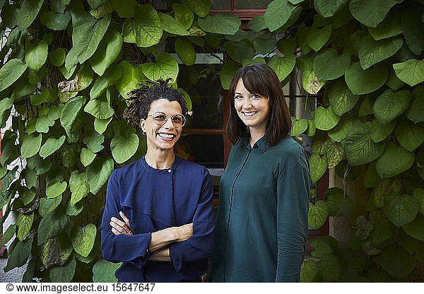 Portrait of smiling female architects standing against creeper plants in backyard