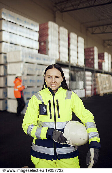 Portrait of smiling female blue-collar worker in protective workwear at industry