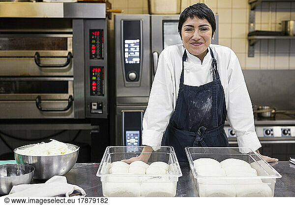 Portrait of smiling female chef with dough in commercial kitchen