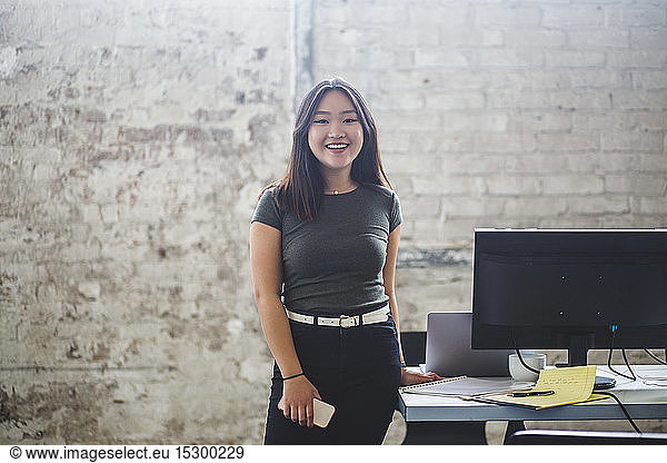 Portrait of smiling female computer programmer standing beside desk at creative office