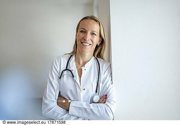Portrait of smiling female doctor leaning against a wall