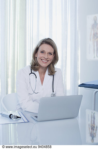 Portrait of smiling female doctor sitting at desk with laptop