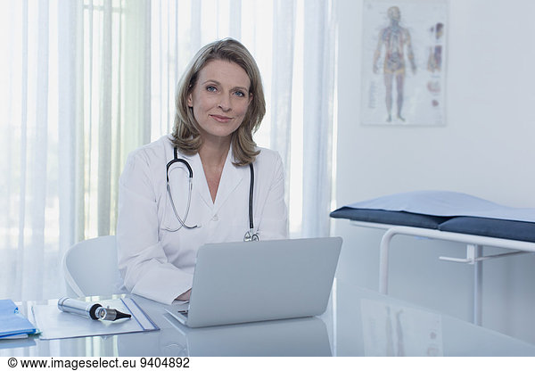 Portrait of smiling female doctor sitting at desk with laptop in office