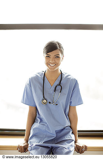 Portrait of smiling female doctor sitting on window sill