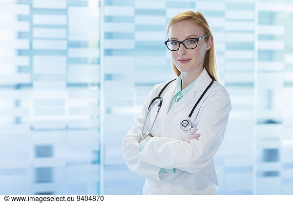 Portrait of smiling female doctor wearing glasses and lab coat standing with arms crossed