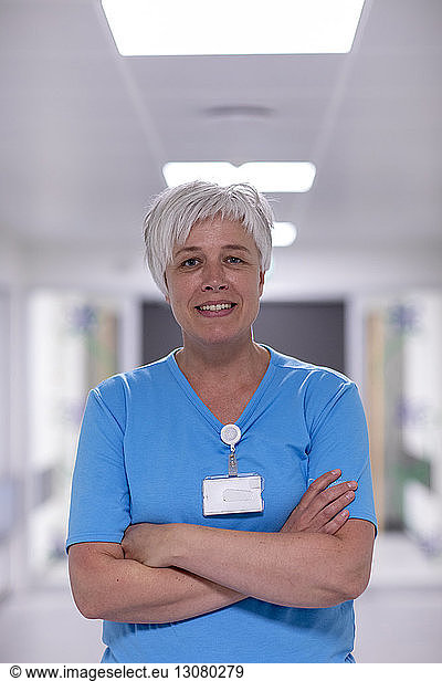 Portrait of smiling female doctor with arms crossed standing in hospital corridor