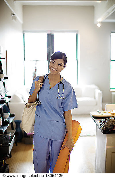 Portrait of smiling female doctor with shoulder bag standing at home