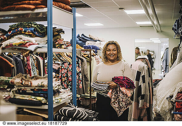 Portrait of smiling female fashion designer holding fabrics while standing at workshop