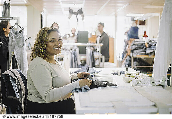 Portrait of smiling female fashion designer sitting at workbench in workshop