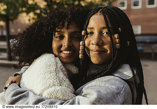 Portrait of smiling female friends embracing each other on footpath