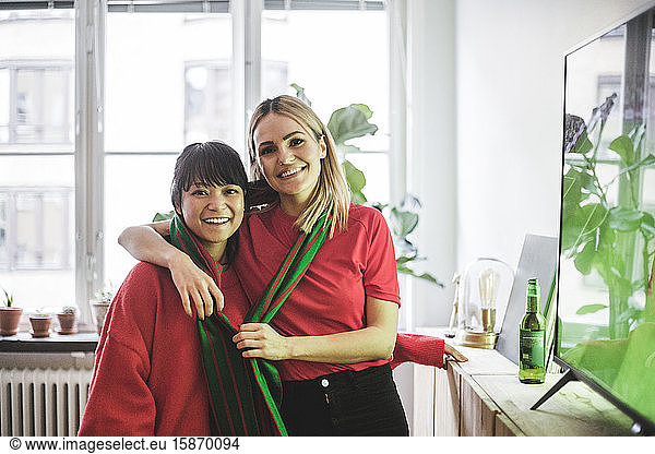 Portrait of smiling female friends standing with arm around at home