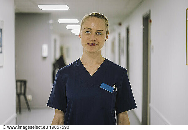 Portrait of smiling female healthcare worker standing in corridor at hospital