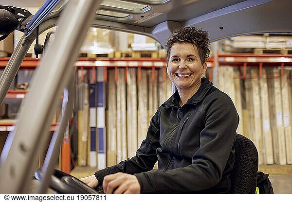 Portrait of smiling female operator driving forklift in lumber industry