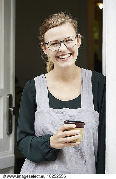 Portrait of smiling female owner having coffee at entrance of art studio