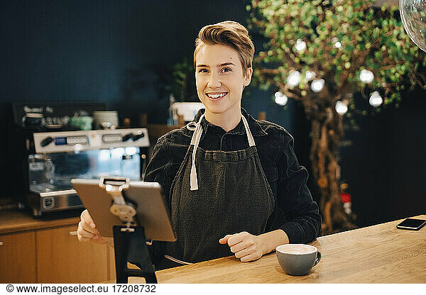 Portrait of smiling female owner with digital tablet in cafeteria