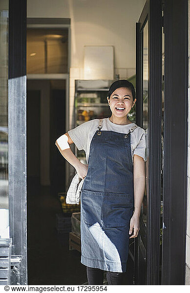 Portrait of smiling female owner with hand on hip standing at entrance of store