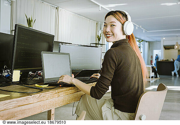 Portrait of smiling female programmer working on laptop in creative office