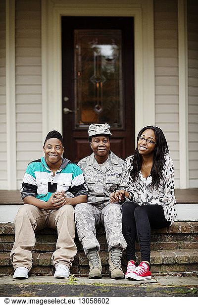 Portrait of smiling female soldier sitting with children outside house