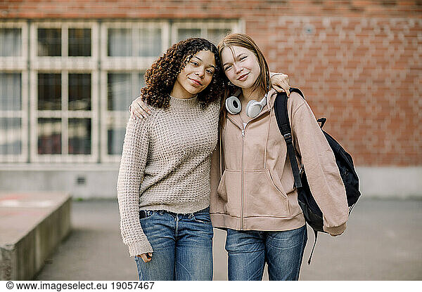 Portrait of smiling female students standing with arms around in high school campus