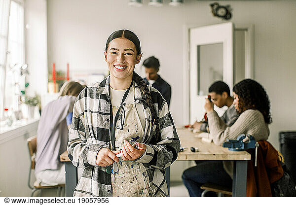 Portrait of smiling female teacher wearing plaid shirt with students in background at carpentry class