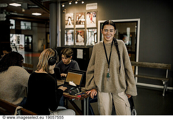 Portrait of smiling female teacher with students using laptops at high school
