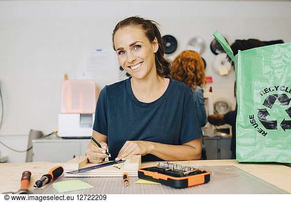 Portrait of smiling female technician working while sitting at workbench in creative office