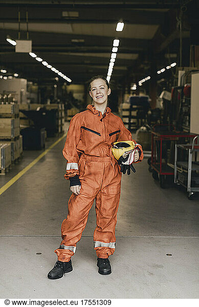 Portrait of smiling female worker in protective workwear standing in factory