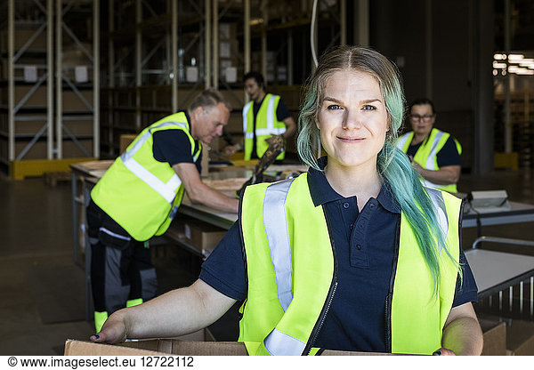Portrait of smiling female worker with dyed hair standing against coworkers in distribution warehouse