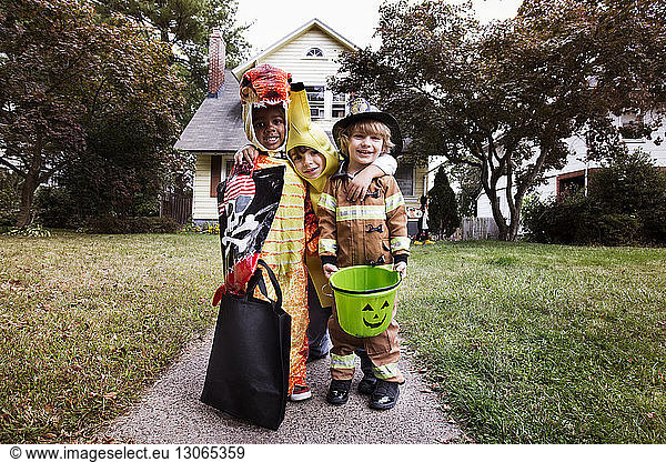 Portrait of smiling friends in Halloween costume standing against house during trick or treating
