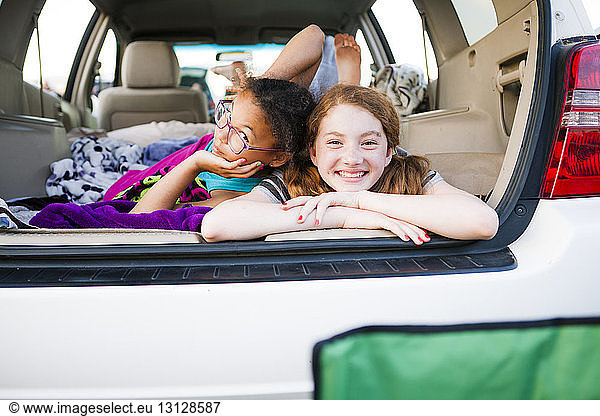Portrait of smiling friends lying in car trunk