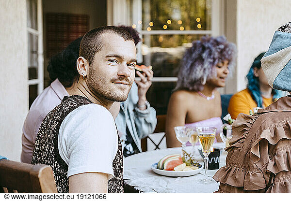 Portrait of smiling gay man with friends at dining table during dinner party in back yard