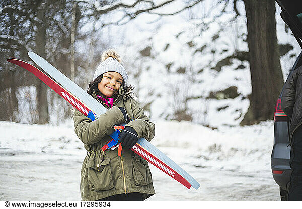 Portrait of smiling girl carrying skis during winter