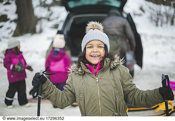 Portrait of smiling girl holding ski poles during winter