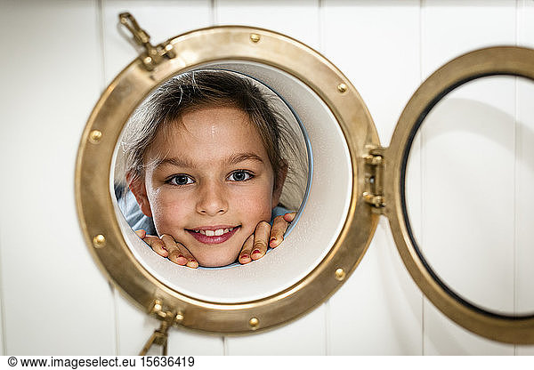 Portrait of smiling girl looking through porthole