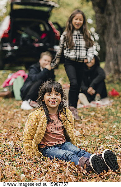 Portrait of smiling girl sitting on autumn leaves during picnic