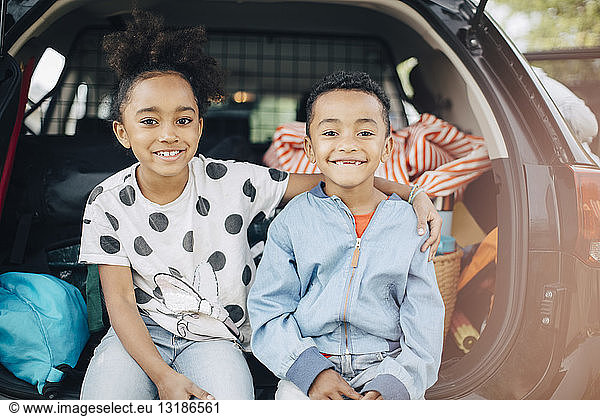 Portrait of smiling girl sitting with arm around on brother in electric car trunk