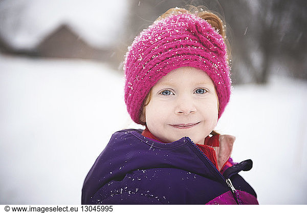 Portrait of smiling girl standing outdoors during snowfall