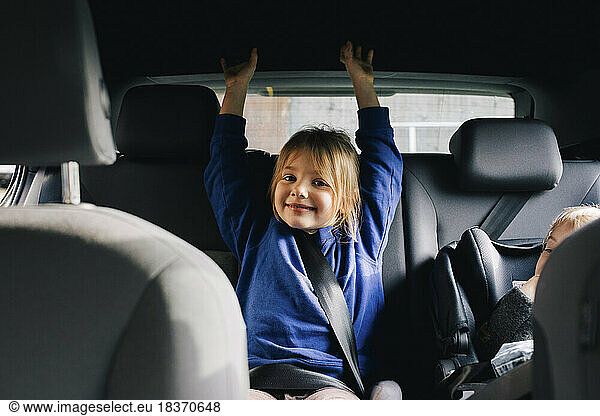 Portrait of smiling girl with arms raised sitting at back seat in car