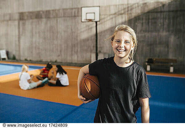 Portrait of smiling girl with basketball at sports court