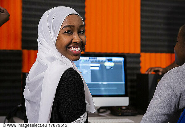 Portrait of smiling girl with hijab sitting in recording studio
