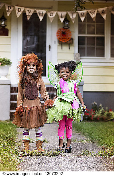 Portrait of smiling girls in Halloween costume standing against house at yard