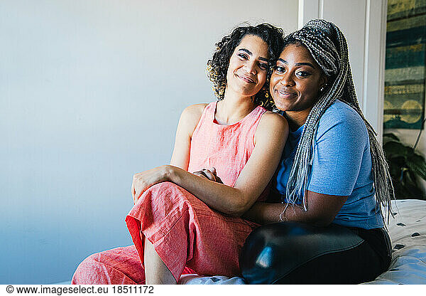 Portrait of smiling lesbian couple sitting on bed at home