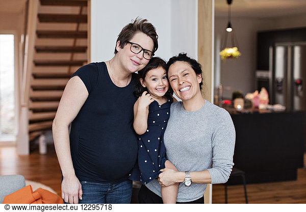Portrait of smiling lesbian couple with daughter in living room at home